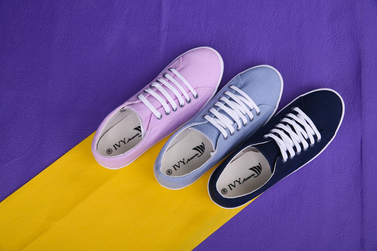 who-we-are Three different colored sneakers displayed on a yellow and purple background, showcasing modern fashion.